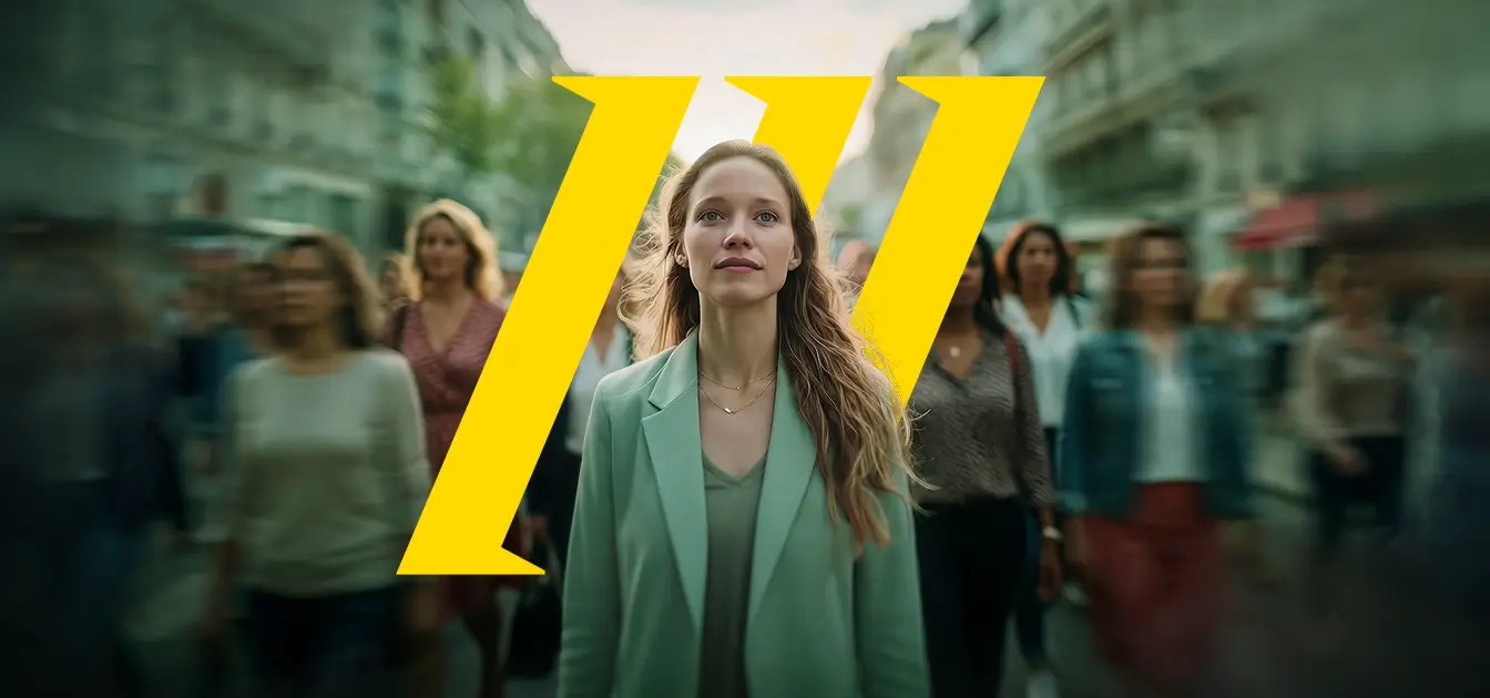 Μια νεαρή γυναίκα στο κέντρο ενός αστικού δρόμου, να περπατά προς τα εμπρός με ήρεμη αλλά αποφασιστική έκφραση. Φορά ανοιχτόχρωμο σακάκι και έχει τα μαλλιά της λυτά. Γύρω της κινούνται πολλοί άνθρωποι, ελαφρώς θολοί, σαν να βρίσκονται σε κίνηση, ενώ εκείνη παραμένει καθαρή και εστιασμένη στο πλάνο.