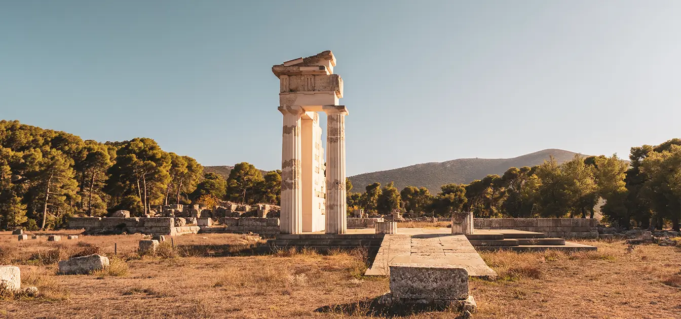 Αρχαιολογικός χώρος με αρχαία πύλη και στήλες σε φυσικό τοπίο με δέντρα και λόφους