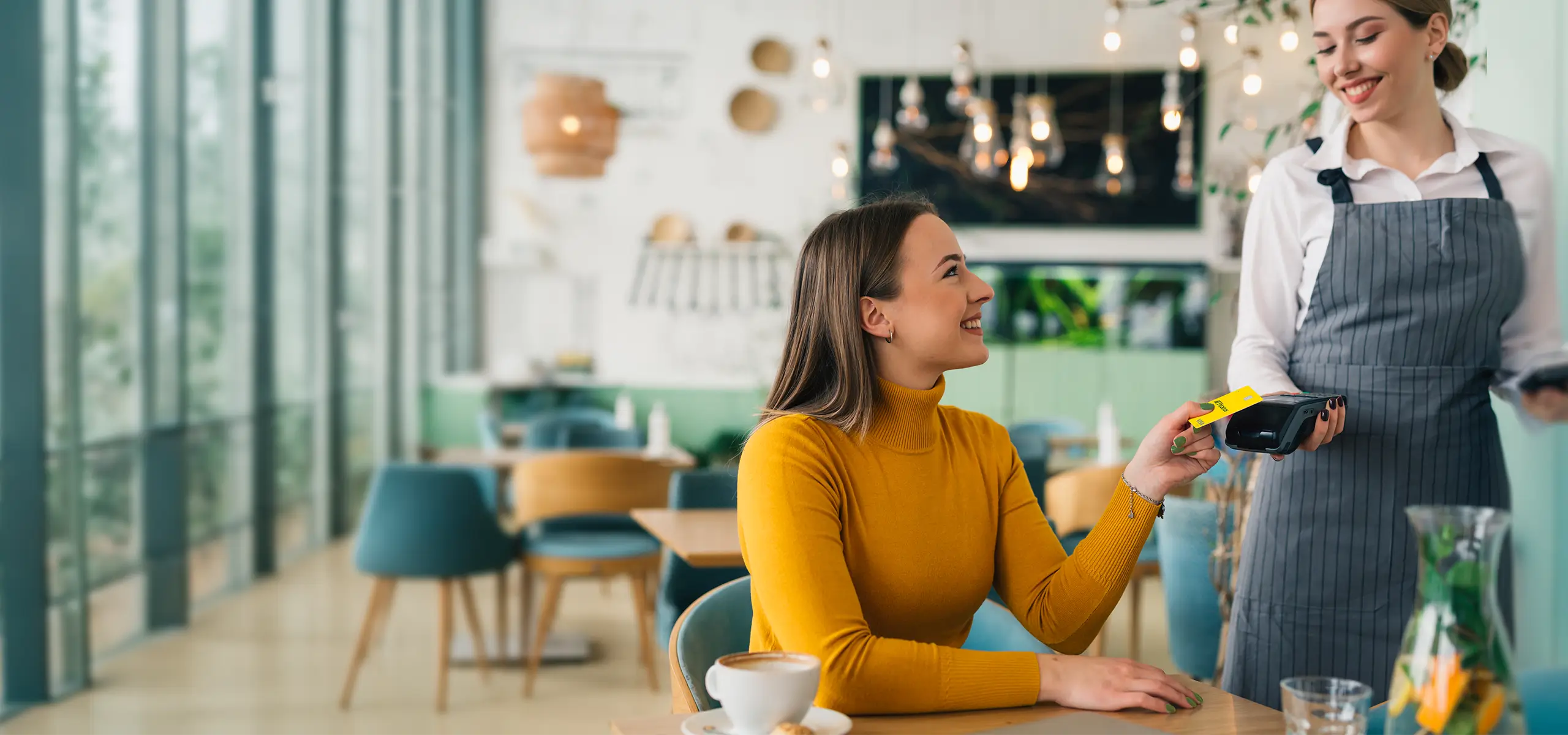 Γυναίκα σε καφέ πληρώνει με κάρτα Πειραιώς σε τερματικό POS που κρατά σερβιτόρα