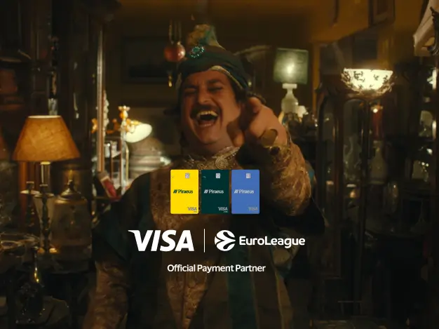 A man in traditional attire laughs and points toward the camera in a warmly lit interior, with Visa and EuroLeague logos